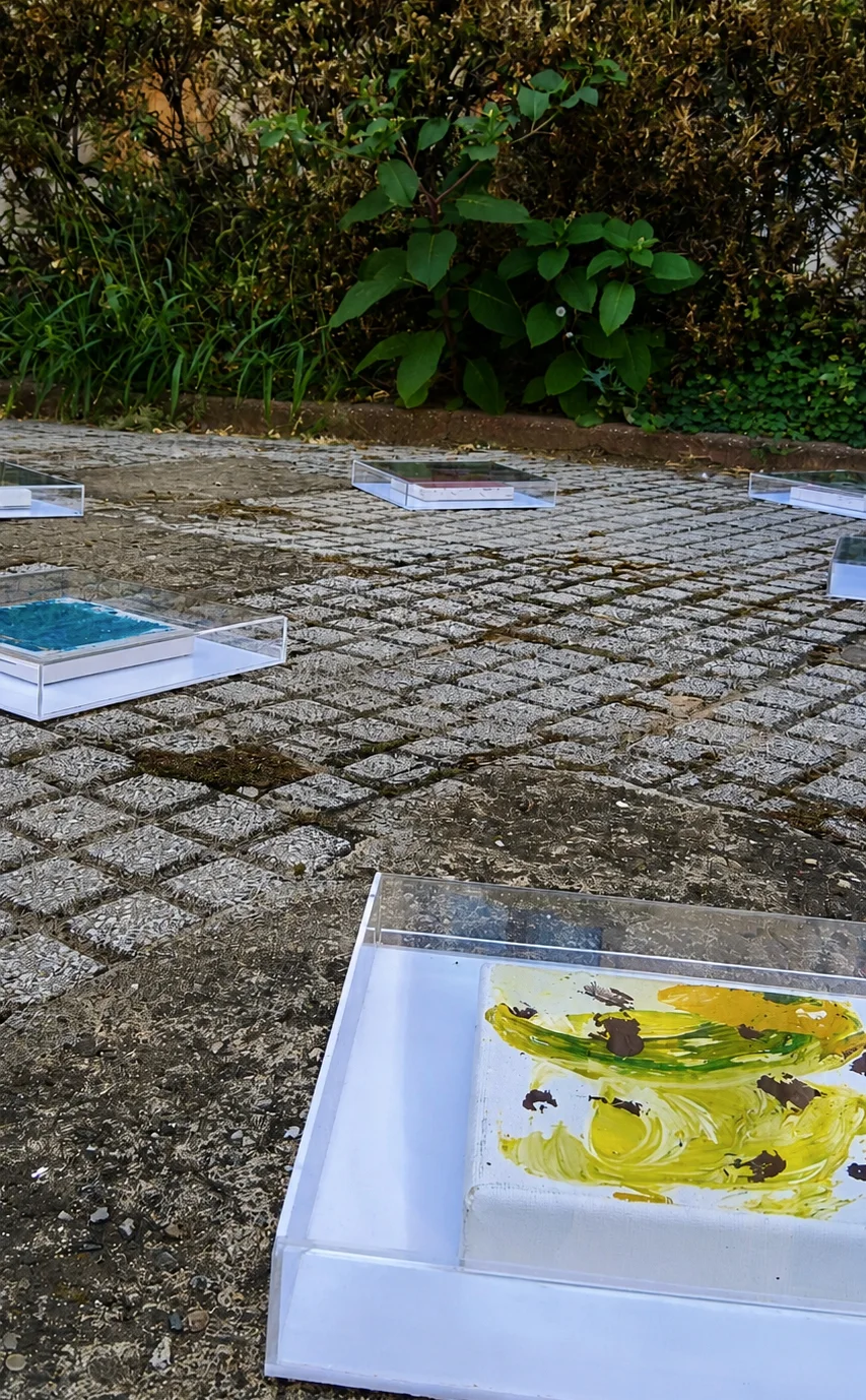 Detail of Adrian Dică’s SEEDS installation, with paintings protected in transparent cases and placed on the courtyard paving at Cantacuzino Palace, Bucharest, 2026